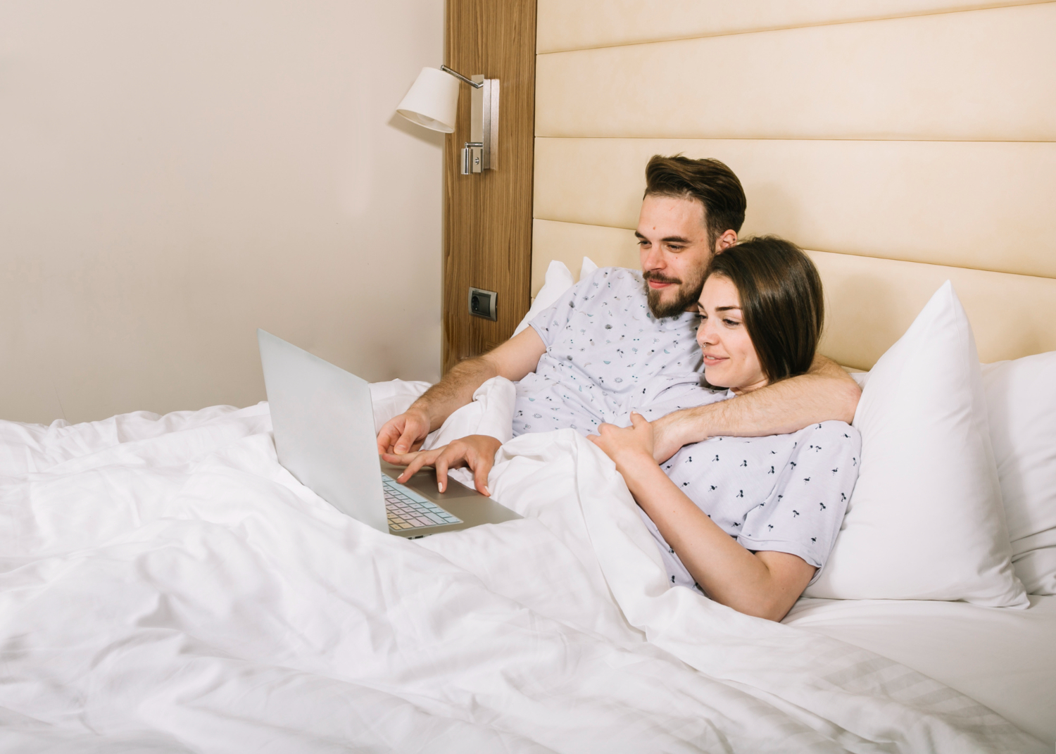 Couple using laptop on bed linens