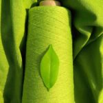 A green thread roll, piece of cloth and a tree leaf showcasing textiles fabric making